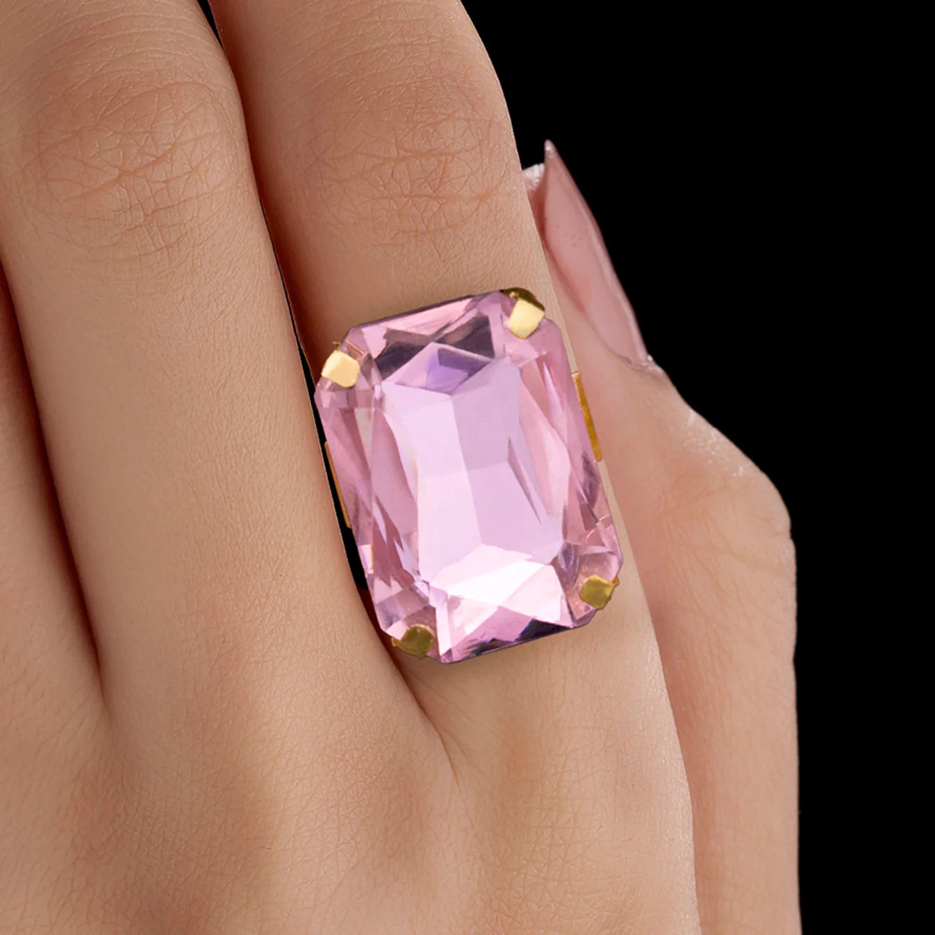 Close-up of a hand wearing an anti-tarnish adjustable  pink crystal ring against a blurred background.
