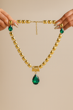 Gold necklace with green gemstones held by hands against a beige background
