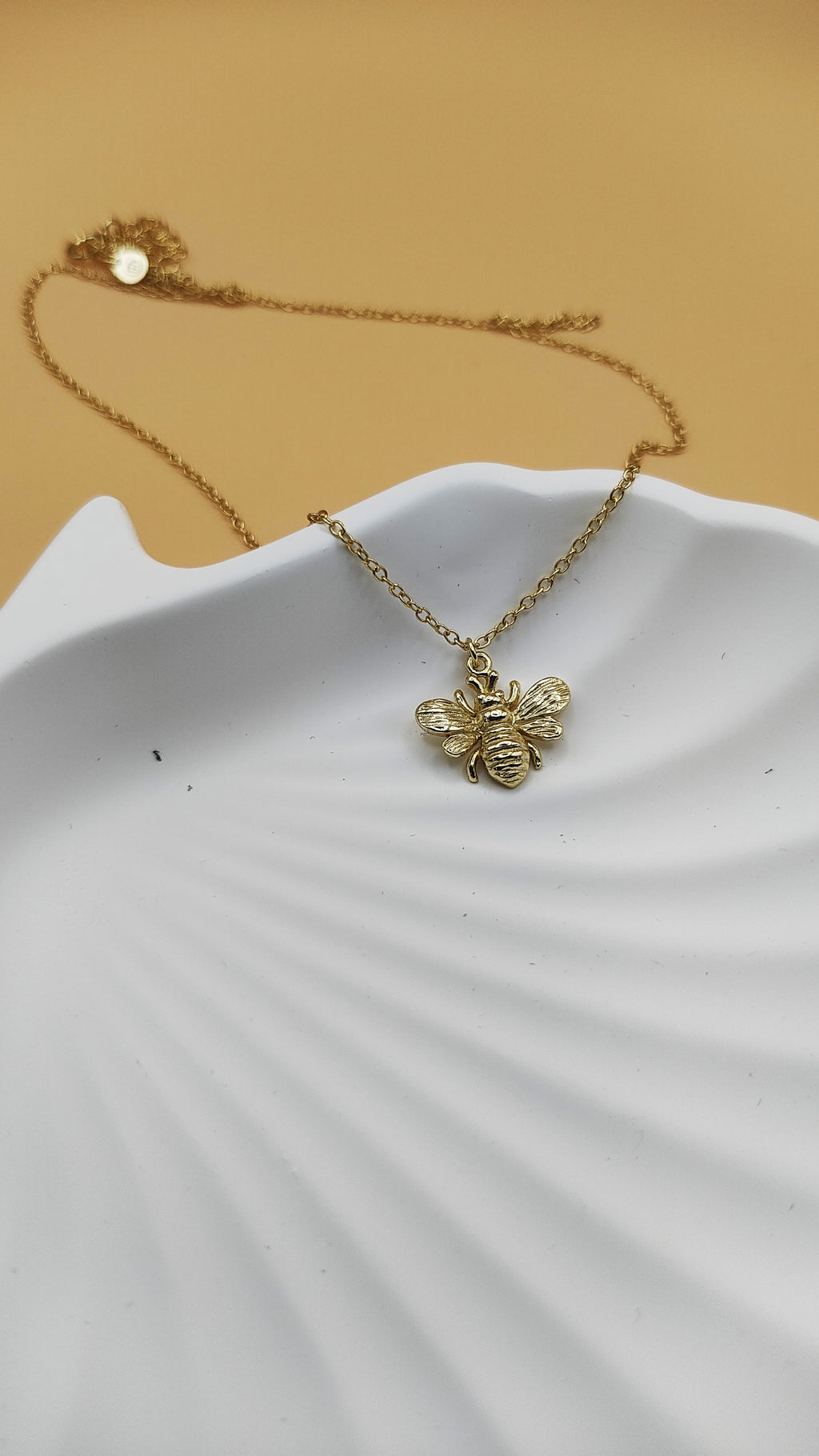 Gold bee necklace on a white dish with a beige background