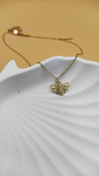 Gold bee necklace on a white dish with a beige background