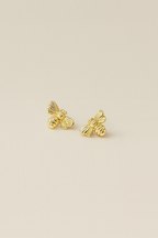 Gold bee-shaped earrings on a beige background