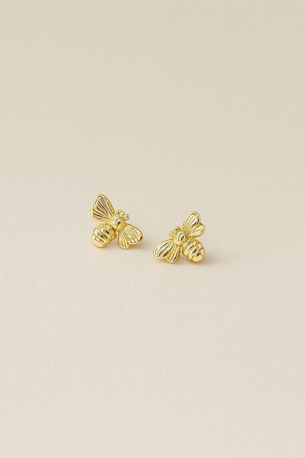 Gold bee-shaped earrings on a beige background