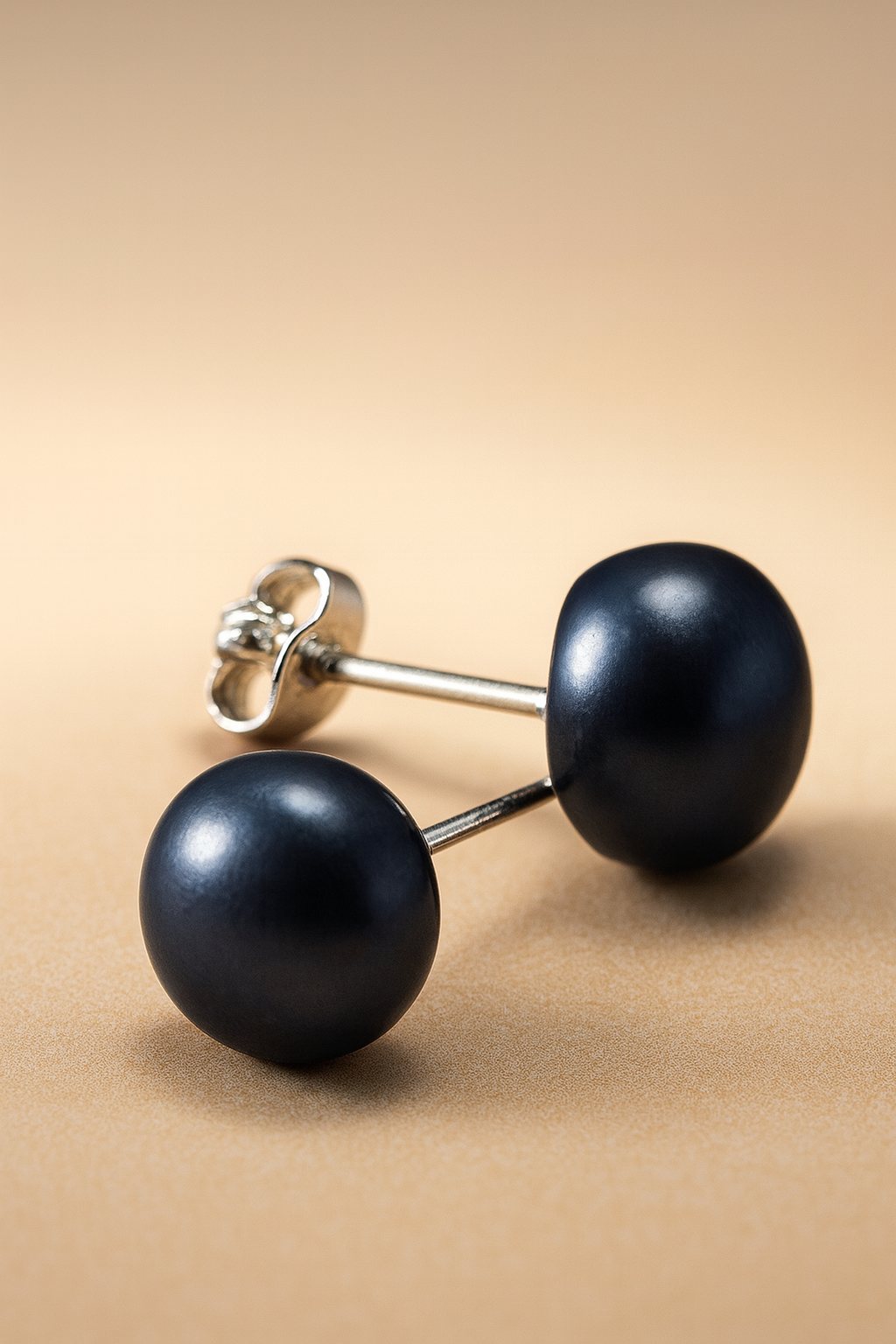 Pair of black pearl earrings on a beige background