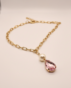Gold chain bracelet with a pink teardrop pendant and pearl on a light background