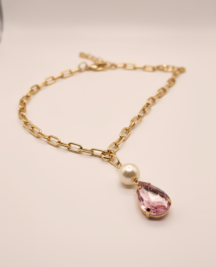 Gold chain bracelet with a pink teardrop pendant and pearl on a light background