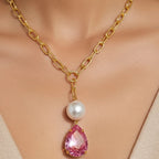 Gold chain necklace with a pink teardrop pendant and pearl on a mannequin.