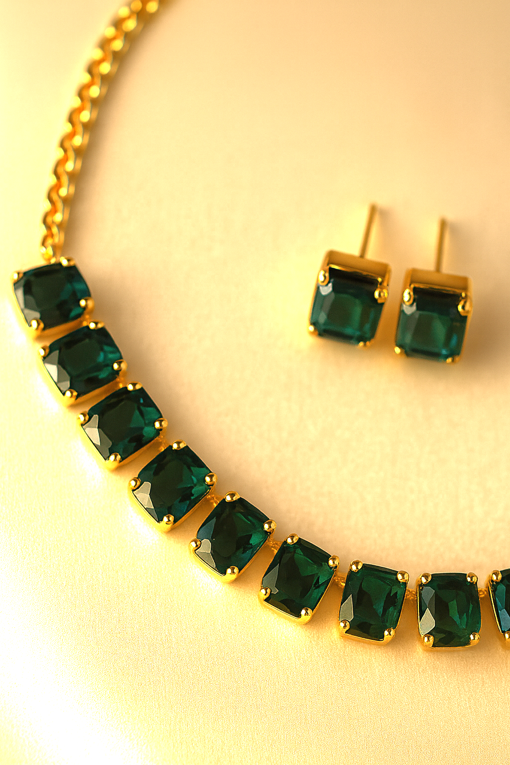 Gold necklace and earrings with green gemstones on a yellow background