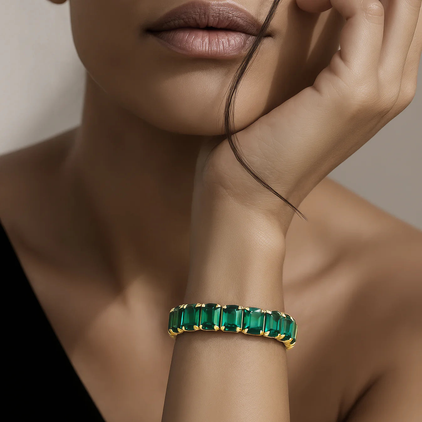 Gold bracelet with emerald stones on a model's wrist against a neutral background