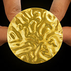 Anti-tarnish gold coin-style ring with an adjustable band and intricate design, held between fingers against a black background.