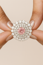 Close-up of a ring with a pink gemstone and diamond surround held between fingers.