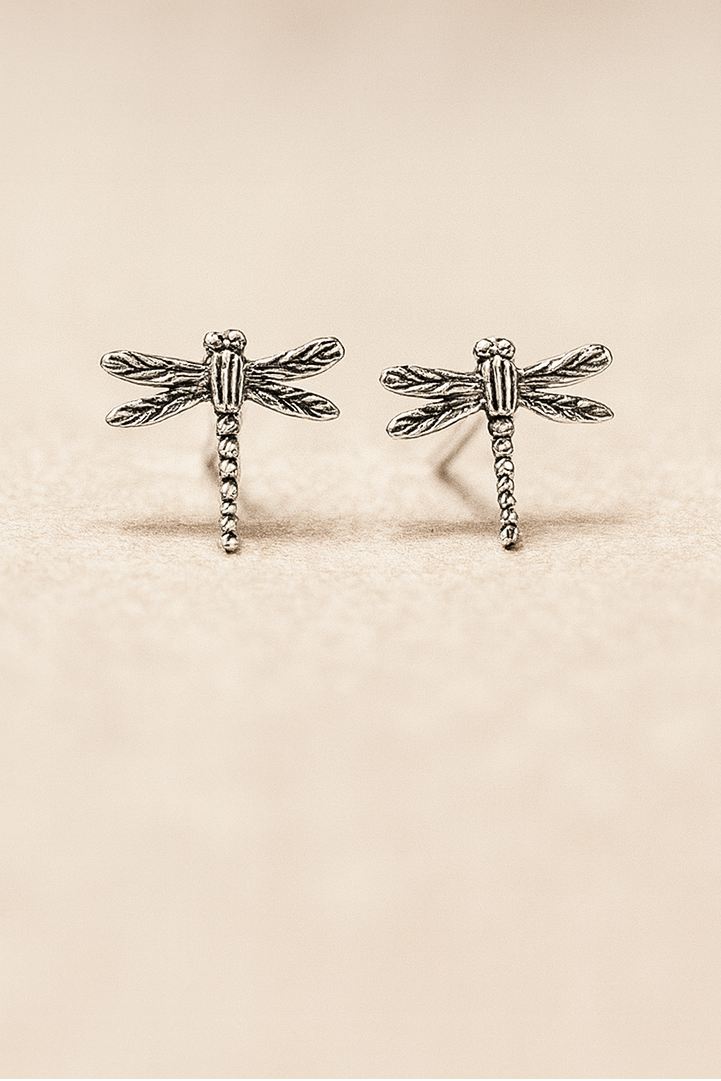 Pair of silver dragonfly-shaped earrings on a beige background