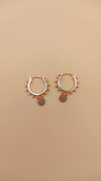Pair of rose gold hoop earrings with small circular designs on a beige background