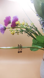 Pair of earrings on a branch with pink flowers and green leaves in the background