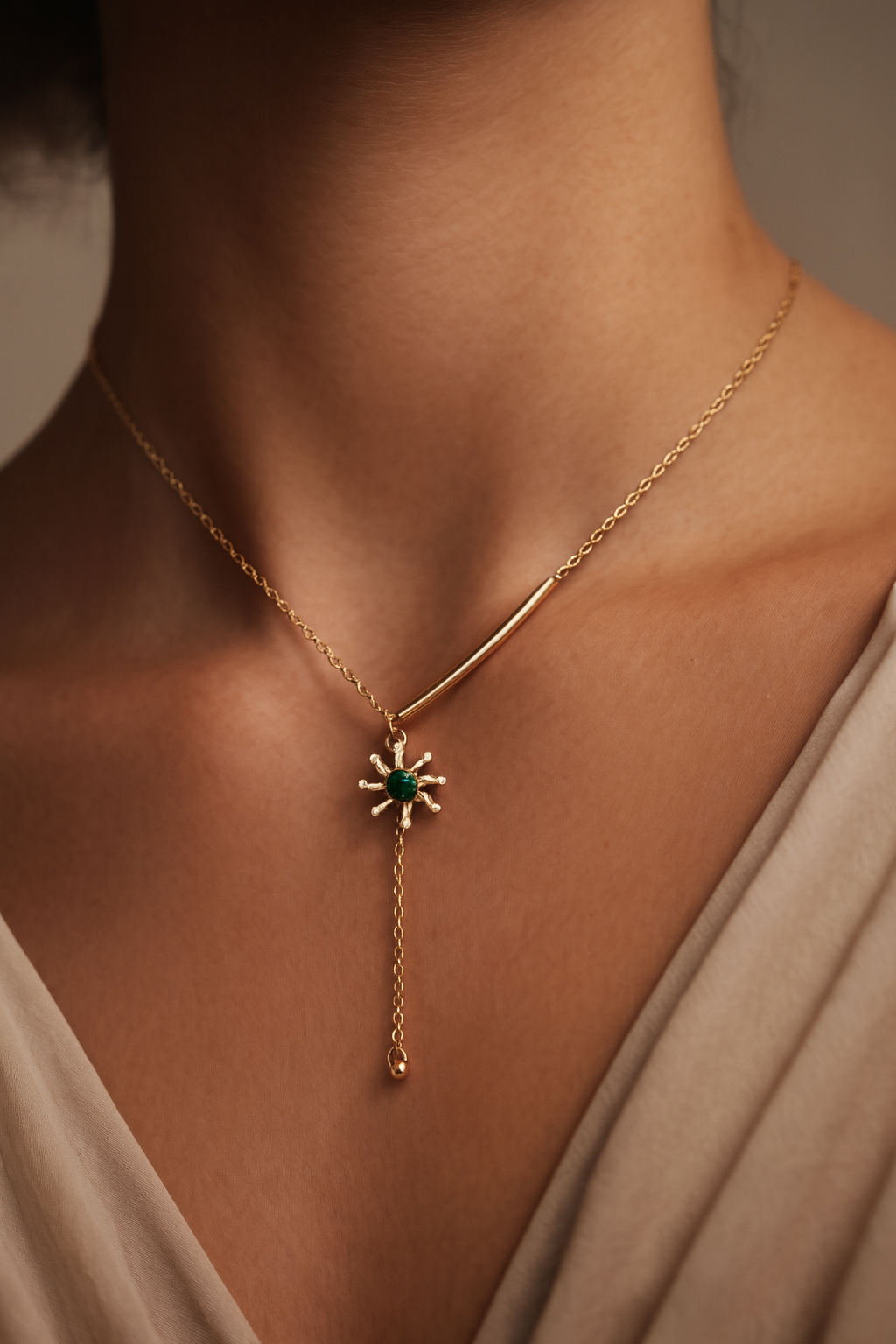 Gold necklace with a green gemstone pendant on a person wearing a beige top.
