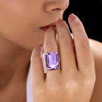 Close-up of a hand wearing an anti-tarnish tanzanite crystal ring against a blurred background.