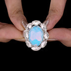 Ring with a blue gemstone held between fingers against a black background