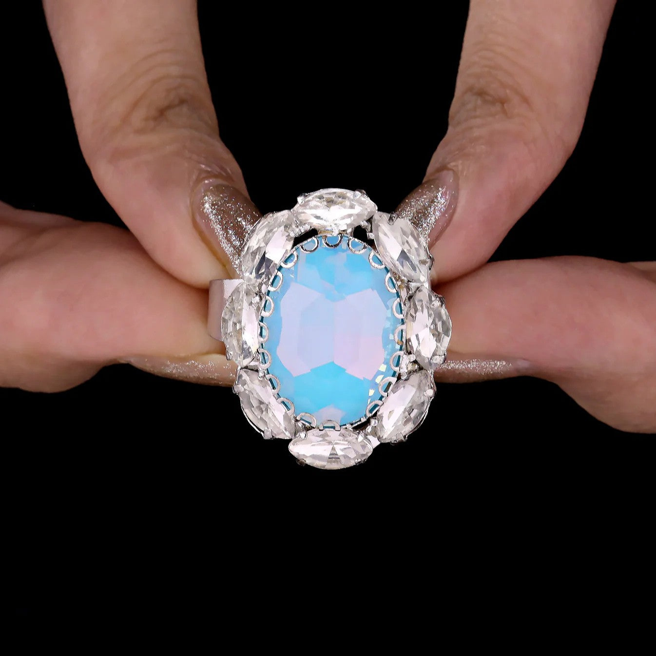 Ring with a blue gemstone held between fingers against a black background
