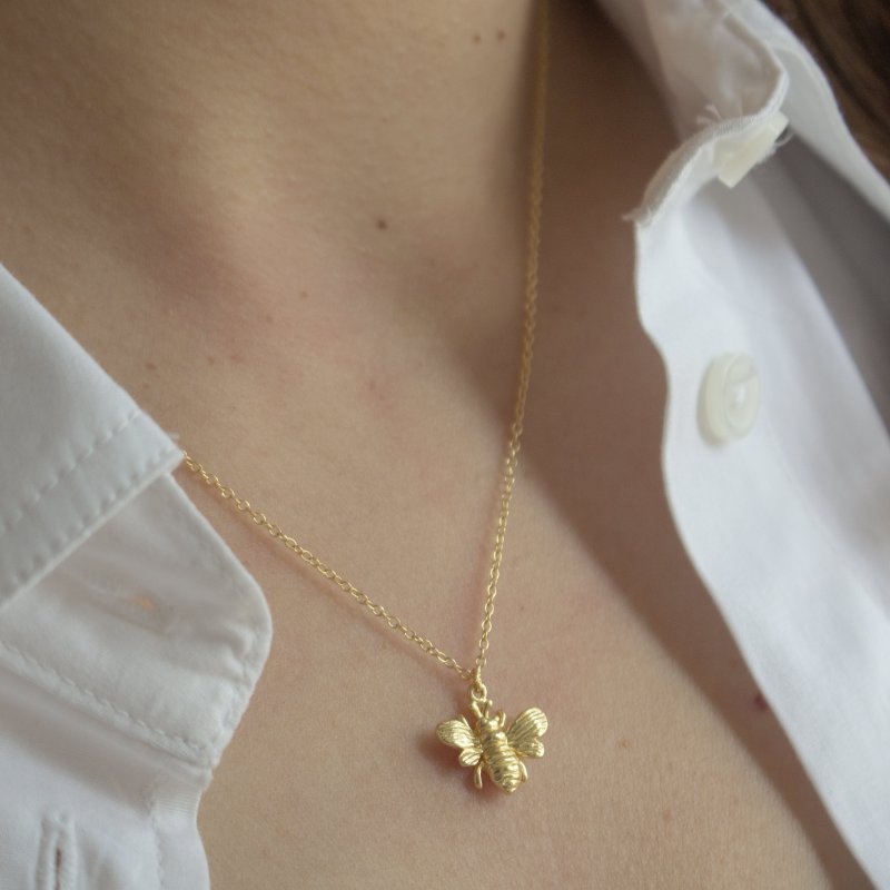 Gold bee necklace on a person wearing a white shirt