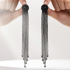 Black beaded tassel earrings held by a hand against a white background