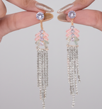 Elegant tassel earrings held by a hand against a neutral background
