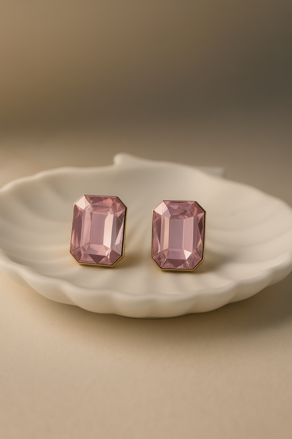 Pair of pink crystal earrings on a white dish with a beige background