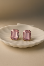 Pair of pink crystal earrings on a white dish with a beige background