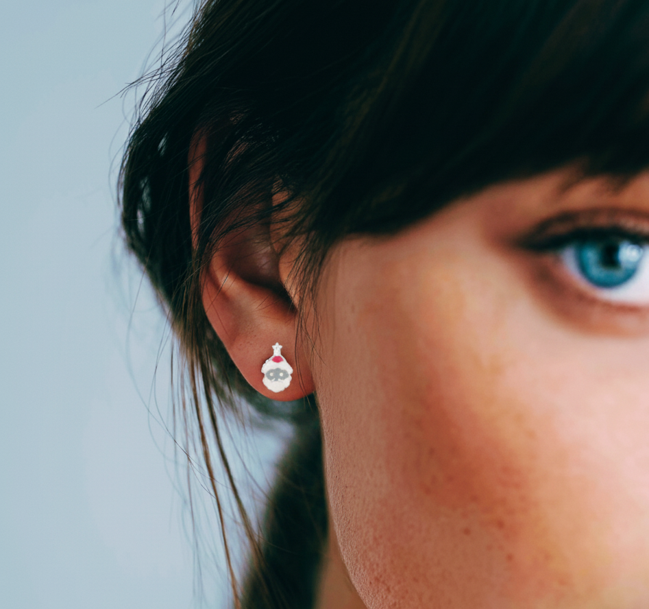 Close-up of a woman's ear wearing a silver santa face studs background.